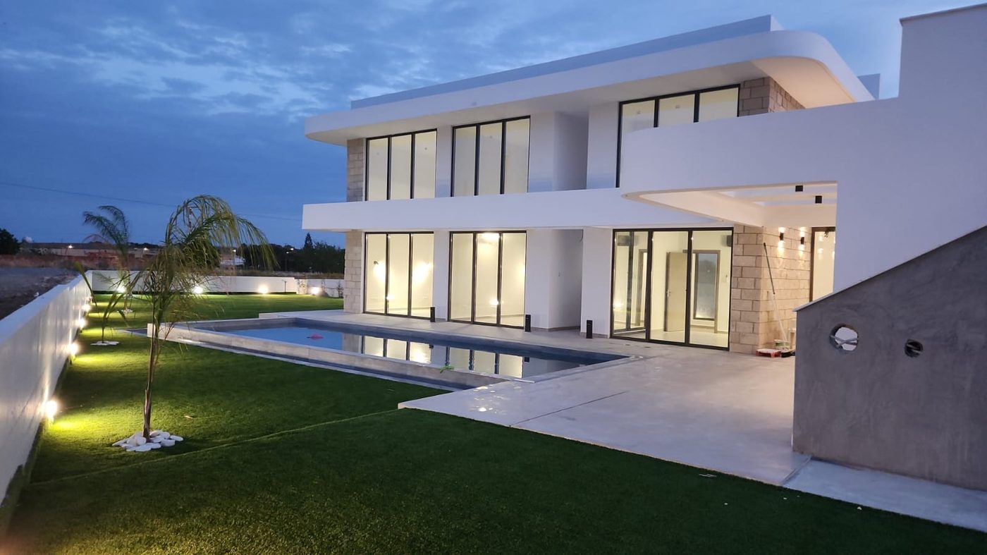The same villa from the garden side at dusk, stone and render facade lit from below